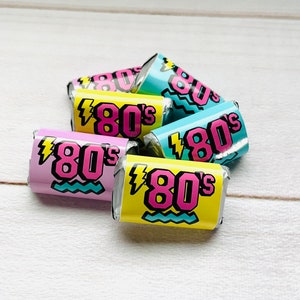 Pu&ograve; includere: Un gruppo di cinque piccoli caramelle avvolti con un tema retr&ograve; degli anni '80. Le caramelle sono avvolte in carta gialla, rosa e blu con un design a forma di fulmine e linea ondulata. Il testo "80's" &egrave; stampato in rosa su ogni caramella.