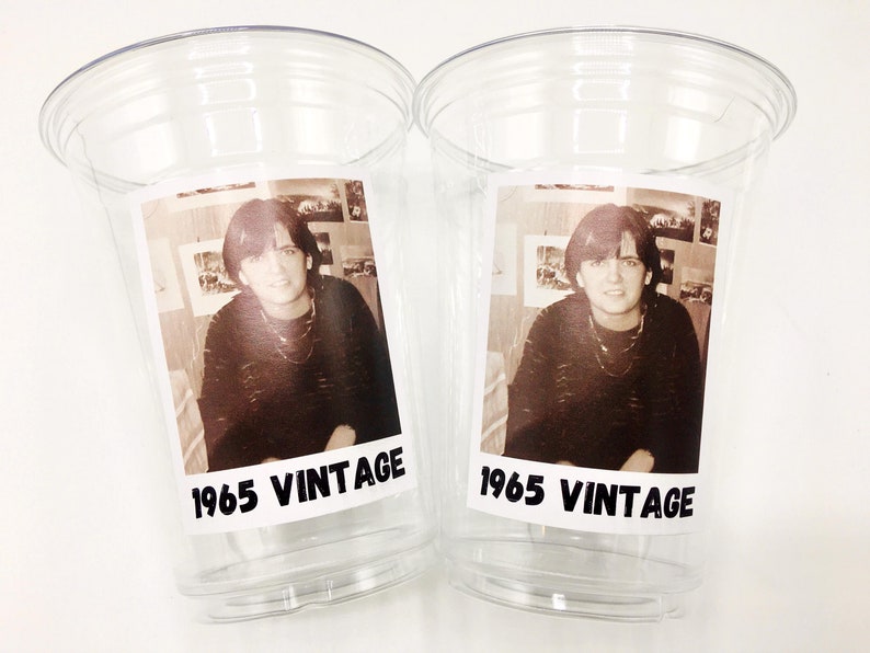 May include: Two clear plastic cups with black and white photos of a person inside. The photos are labelled "1965 Vintage".
