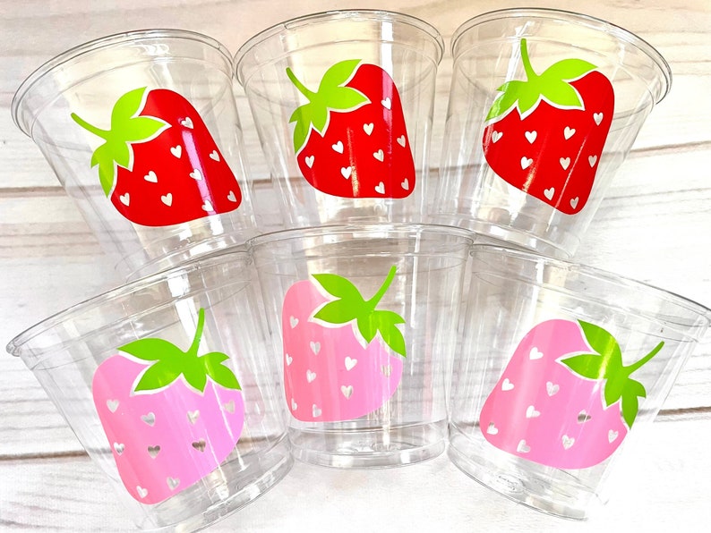 Op de afbeelding: Zes doorzichtige plastic bekers met aardbeides ontwerpen. De aardbeien zijn rood en roze met witte hartjes en groene bladeren.