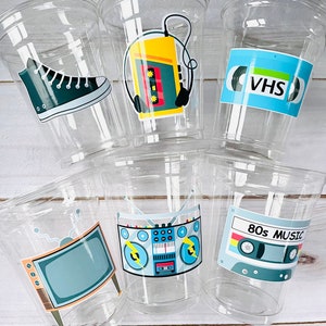 K&ouml;nnte beinhalten: Sechs durchsichtige Plastikbecher mit bunten Aufklebern im 80er-Jahre-Stil. Die Aufkleber zeigen ein Paar Turnschuhe, ein Kassettenband, eine Boombox, einen Fernseher und ein VHS-Band.