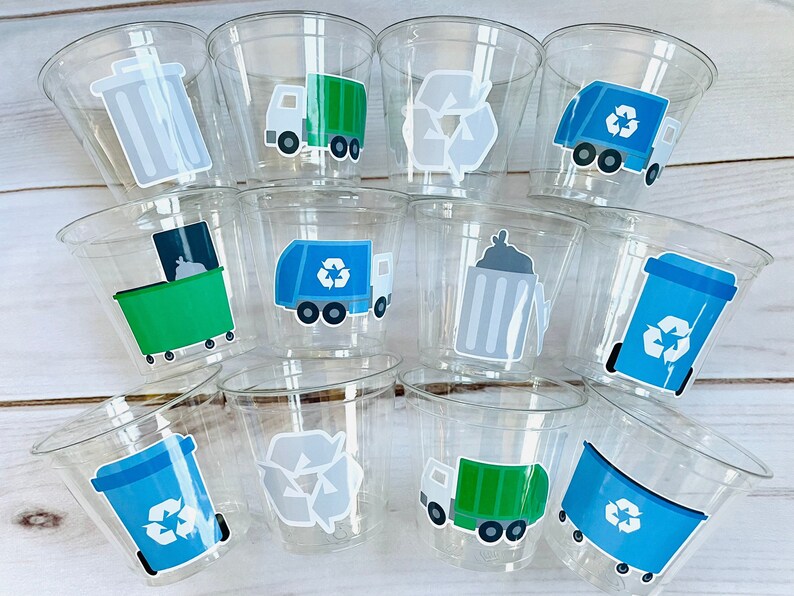 May include: Twelve clear plastic cups with various recycling themed stickers. The stickers feature a green garbage truck, a blue recycling bin, a gray trash can, and a recycling symbol.
