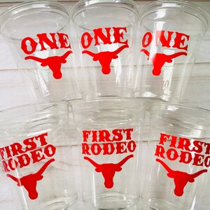 K&ouml;nnte beinhalten: Sechs durchsichtige Plastikbecher mit roten und wei&szlig;en Designs. Drei Becher sagen "ONE" mit einem roten Longhorn-Stierkopf. Drei Becher sagen "FIRST RODEO" mit einem roten Longhorn-Stierkopf.