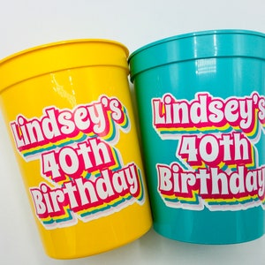 Puede incluir: Dos vasos de fiesta de pl&aacute;stico, uno amarillo y otro turquesa, con el texto "Lindsey's 40th Birthday" en una fuente retro colorida. Los vasos est&aacute;n dise&ntilde;ados para una celebraci&oacute;n de cumplea&ntilde;os.