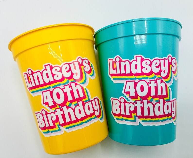 Puede incluir: Dos vasos de fiesta de pl&aacute;stico, uno amarillo y otro turquesa, con el texto "Lindsey's 40th Birthday" en una fuente retro colorida. Los vasos est&aacute;n dise&ntilde;ados para una celebraci&oacute;n de cumplea&ntilde;os.