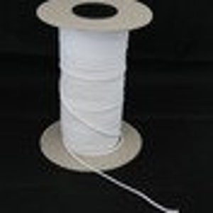 Peut inclure: Une bobine de cordon élastique blanc. Le cordon est étroitement enroulé autour d'une bobine en carton. Le cordon élastique est d'un blanc éclatant et semble neuf et inutilisé. La bobine est posée sur une surface noire.