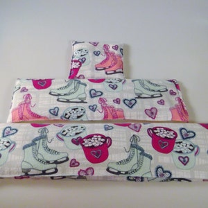 May include: Three white fabric heat packs with different designs. The top pack has a pink and white design with ice skates and hearts. The middle pack has a pink and white design with ice skates and hearts. The bottom pack has a pink and white design with mugs of hot chocolate and hearts.