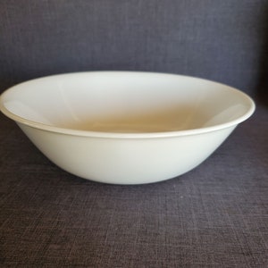 May include: A white, round serving bowl with a wide rim. The bowl is made of a smooth, solid material and is set against a dark gray background. This versatile bowl is suitable for serving salads, pasta, or other dishes.