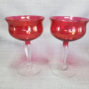 May include: Two clear glass stemmed goblets with a deep red, almost burgundy, colored bowl. The goblets are clear glass with a frosted stem.