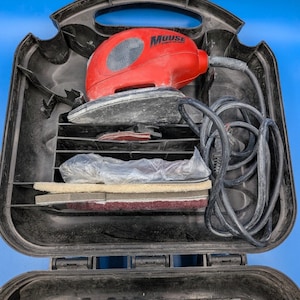 May include: A red Mouse sander with a black case. The sander has a gray sanding pad and a black power cord. The case contains sanding pads and accessories. The case is open, revealing the contents.
