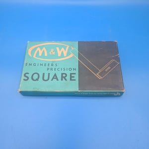 May include: A vintage M&W Engineers' Precision Square box. The box is divided into two sections: a teal section with the brand name and product description, and a dark gray section with a diagram of the square. The box is on a blue background.
