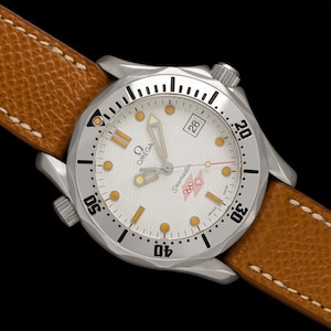 May include: A silver Omega Seamaster watch with a white dial, featuring gold-toned hands and markers, and a date window at the 3 o'clock position. The watch has a brown leather strap with white stitching. The watch is set against a black background.