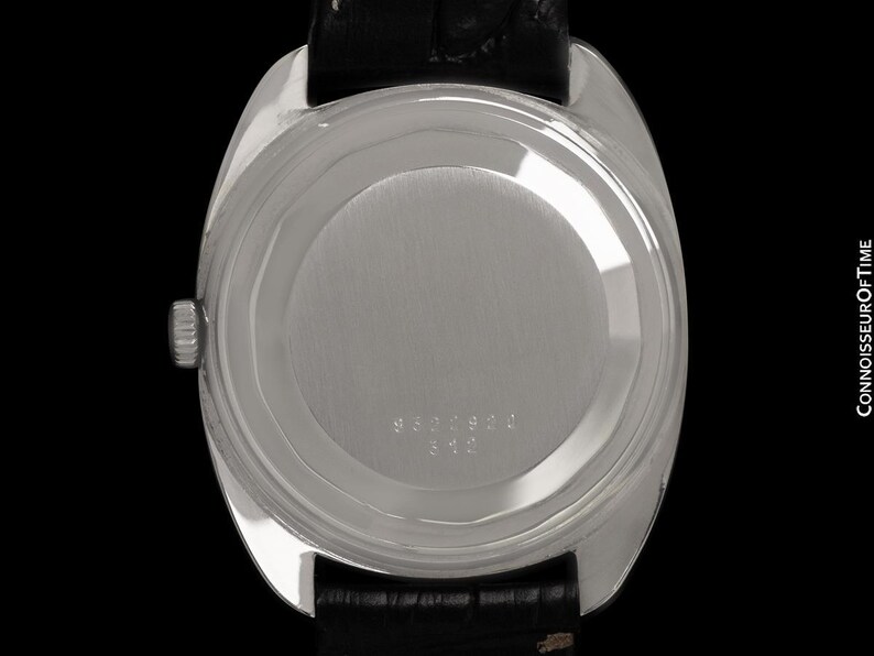 May include: A silver-toned wristwatch with a black leather band. The watch case back features a circular design with engraved numbers. The watch is set against a black background.