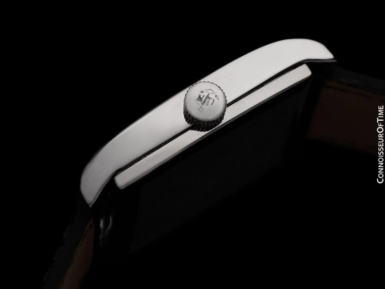 K&ouml;nnte beinhalten: Nahaufnahme einer silbernen Armbanduhr mit braunem Lederarmband. Die Uhr hat ein rechteckiges Zifferblatt und eine strukturierte Krone. Der Hintergrund ist schwarz. Der Text "CONNOISSEUROFTIME" ist auf der rechten Seite sichtbar.