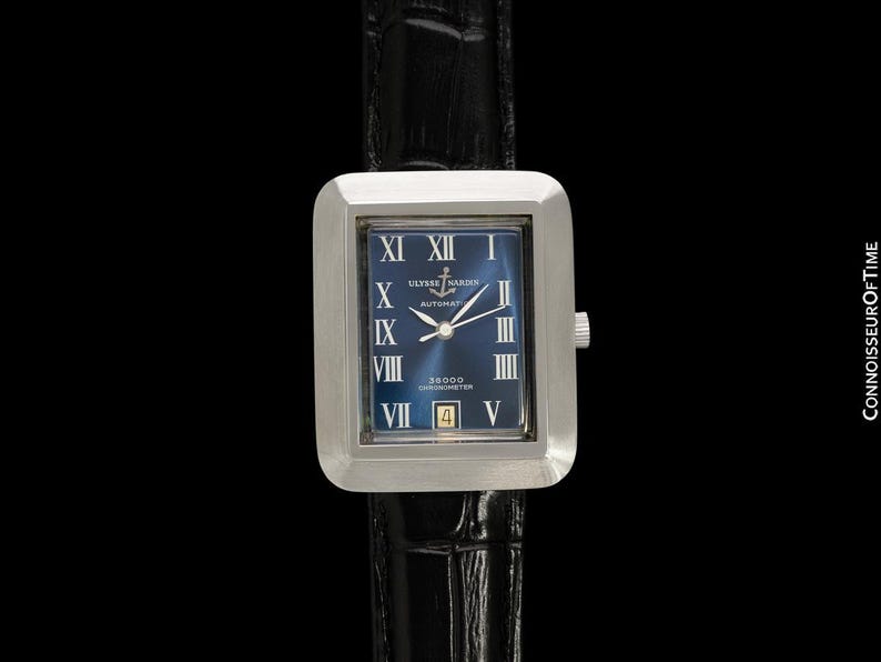 May include: A rectangular silver wristwatch with a blue face and Roman numeral hour markers. The watch has a black leather band and the text "ULYSSE NARDIN AUTOMATIC" is visible on the watch face. The watch also has a date display.