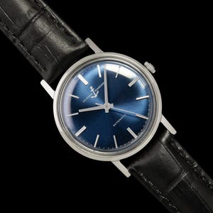 May include: A silver-cased wristwatch with a deep blue dial and a black leather band. The watch face features silver hour markers and hands. The watch is an automatic model, as indicated on the dial. The band has a crocodile pattern.