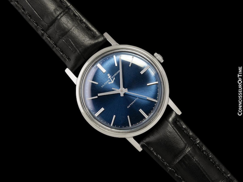 May include: A silver-cased wristwatch with a deep blue dial and a black leather band. The watch face features silver hour markers and hands. The watch is an automatic model, as indicated on the dial. The band has a crocodile pattern.