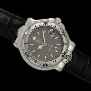 May include: A silver-toned TAG Heuer Professional watch with a black dial and luminous markers. The watch features a rotating bezel and is set on a black leather strap. The watch is a classic timepiece.