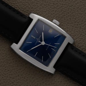 K&ouml;nnte beinhalten: Eine quadratische Armbanduhr mit dunkelblauem Zifferblatt und silbernen Zeigern. Die Uhr hat ein silbernes Geh&auml;use und ein schwarzes Lederarmband. Das Datum wird bei 3 Uhr angezeigt. Automatikwerk.