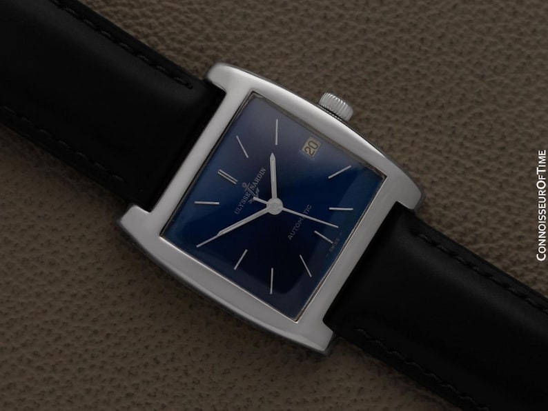 K&ouml;nnte beinhalten: Eine quadratische Armbanduhr mit dunkelblauem Zifferblatt und silbernen Zeigern. Die Uhr hat ein silbernes Geh&auml;use und ein schwarzes Lederarmband. Das Datum wird bei 3 Uhr angezeigt. Automatikwerk.