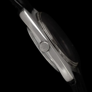 May include: A close-up side view of a silver wristwatch with a black watch face and a black leather strap. The watch has a round face and a silver crown. The text "CONNOISSEUROFTIME" is visible on the right side.
