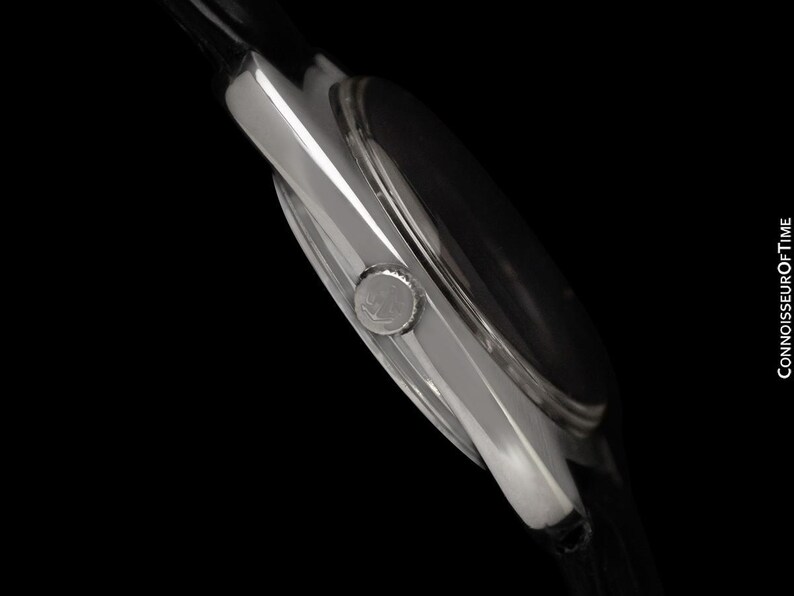 May include: A close-up side view of a silver wristwatch with a black watch face and a black leather strap. The watch has a round face and a silver crown. The text "CONNOISSEUROFTIME" is visible on the right side.