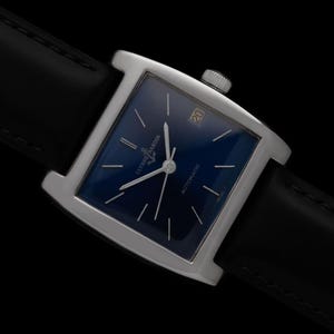 May include: A square-faced wristwatch with a deep blue dial and silver hands. The watch has a silver case and a black leather strap. The date is displayed at the 3 o'clock position. The watch is labeled "Ulysse Nardin Automatic".