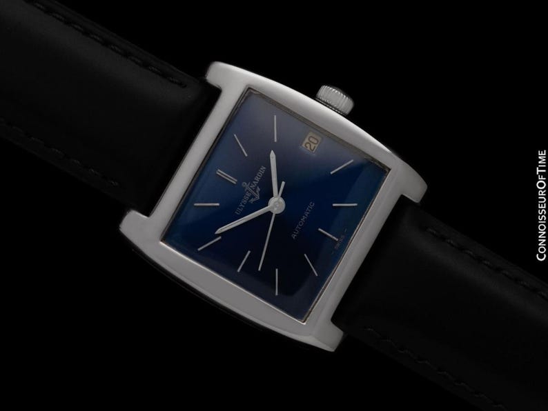 K&ouml;nnte beinhalten: Eine quadratische Armbanduhr mit tiefblauem Zifferblatt und silbernen Zeigern. Die Uhr hat ein silbernes Geh&auml;use und ein schwarzes Lederarmband. Das Datum wird auf 3 Uhr angezeigt. Die Uhr ist mit "Ulysse Nardin Automatic" beschriftet.