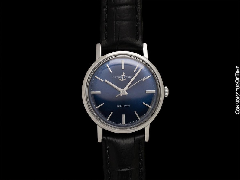 May include: A vintage wristwatch with a dark blue face and silver hands and markers. The watch has a silver case and a black leather band. The watch face features the text "ULYSSE NARDIN" and "AUTOMATIC".