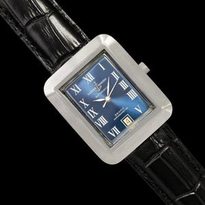 May include: A rectangular stainless steel watch with a blue face and Roman numeral hour markers. The watch features a date window at the 4 o'clock position and is set on a black leather band. The watch face has the text "Ulysse Nardin" and "Automatic".