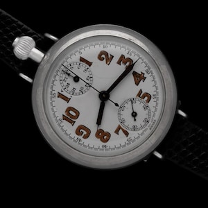 Puede incluir: Un reloj de pulsera cronógrafo plateado con una esfera blanca y números naranjas. El reloj tiene una correa de cuero negra.