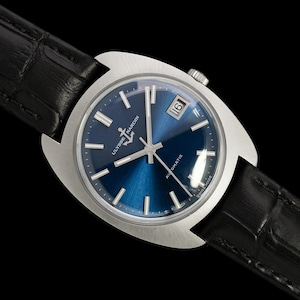 May include: A stainless steel Ulysse Nardin automatic watch with a blue dial and a black leather band. The watch features a date display at the 3 o'clock position and silver hour markers. The watch is set against a black background.
