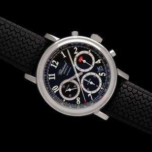 May include: A Chopard Geneve automatic chronograph watch with a round silver-tone stainless steel case, a dark blue dial featuring white Arabic numerals, three sub-dials, a date window, and a black rubber strap with a textured tyre tread pattern.