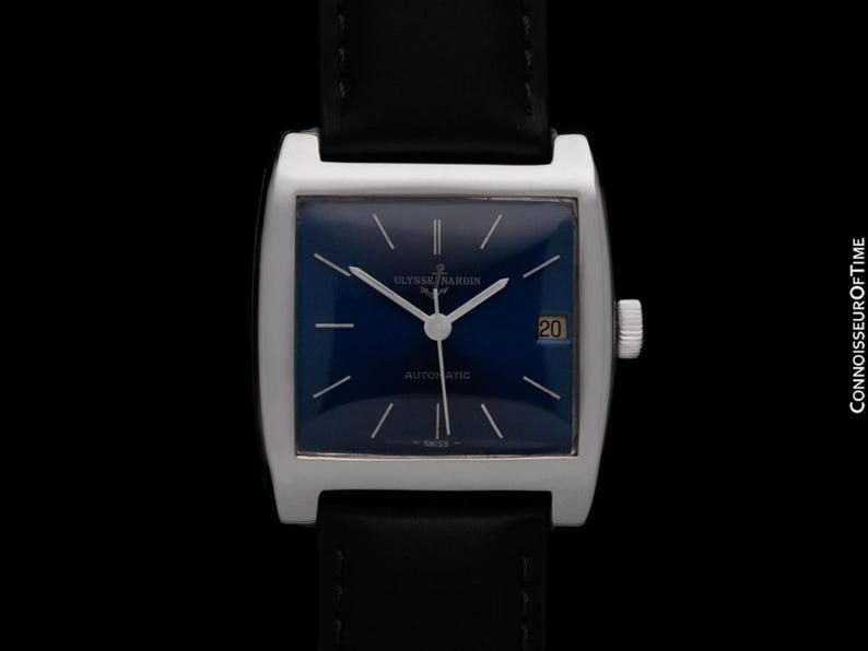 K&ouml;nnte beinhalten: Eine silberfarbene rechteckige Uhr mit dunkelblauem Zifferblatt und schwarzem Lederarmband. Das Zifferblatt hat silberne Zeiger und Markierungen, ein Datumsfenster bei 3 Uhr und den Text "AUTOMATIC". Die Uhr ist vor schwarzem Hintergrund.