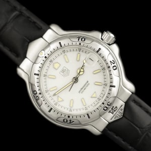 May include: A silver TAG Heuer professional watch with a white face and black leather band. The watch face displays the text "professional 200 METERS". The watch has a rotating bezel and is set against a black background.