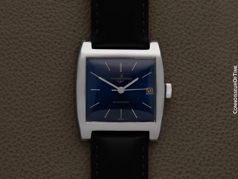 K&ouml;nnte beinhalten: Eine Vintage-Armbanduhr mit einem quadratischen, silberfarbenen Geh&auml;use und einem tiefblauen Zifferblatt. Die Uhr hat ein schwarzes Lederarmband und eine Datumsanzeige bei 3 Uhr. Das Zifferblatt hat silberfarbene Zeiger und Markierungen.