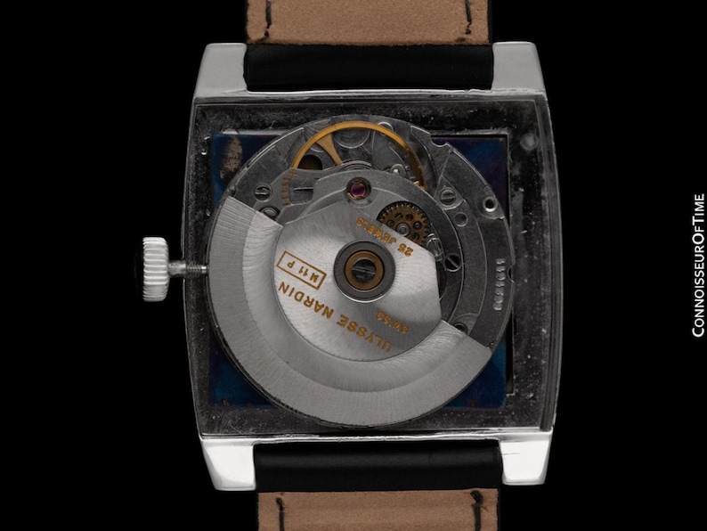 K&ouml;nnte beinhalten: Nahaufnahme einer rechteckigen silbernen Armbanduhr mit braunem Lederarmband. Das transparente Zifferblatt zeigt die komplizierten Innenmechanismen, einschlie&szlig;lich Zahnr&auml;dern und einem Rotor. Die Uhr ist mit "Ulysse Nardin" beschriftet.