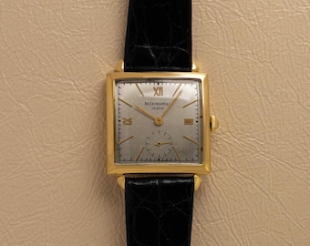 May include: A gold-toned rectangular wristwatch with a silver face and black leather band. The watch face features Roman numerals and the brand name "Patek Philippe & Geneve". The watch has a small seconds dial and gold hands.