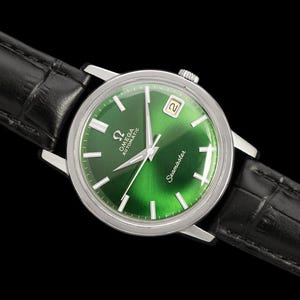 May include: A vintage Omega Seamaster automatic watch with a vibrant green dial and silver hands. The watch features a date window at the 3 o'clock position and is set on a black leather strap. The watch case is silver and the watch is set against a black background.