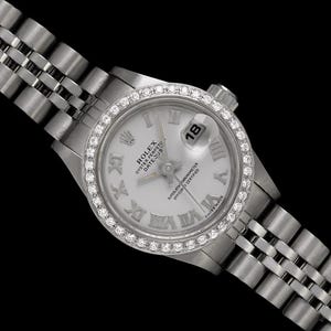 May include: A silver Rolex Oyster Perpetual Datejust watch with a diamond-encrusted bezel. The watch has a white dial with Roman numeral hour markers and a date display at the 3 o'clock position. The watch band is a silver jubilee style.