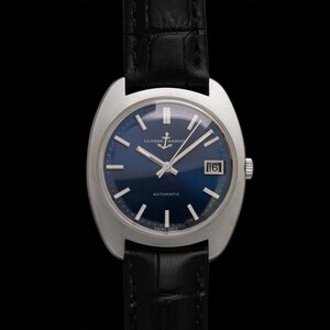 May include: A vintage Ulysse Nardin automatic wristwatch with a dark blue dial and silver hands and markers. The watch has a date window at the 3 o'clock position and is set on a black leather strap. The watch case is silver and has a unique shape.