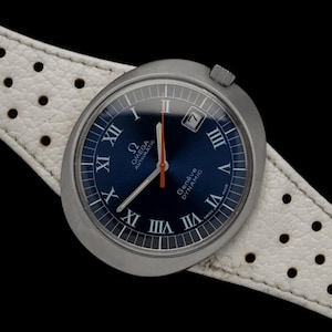May include: A silver Omega Genève Dynamic automatic wristwatch with a blue face and white markings. The watch has a white leather band with a perforated pattern.