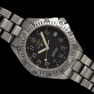 May include: A Breitling 1884 automatic wristwatch with a black dial and silver-tone stainless steel band. The watch features luminous hands and markers, a date display, and a rotating bezel. The watch is water-resistant to 300 meters.