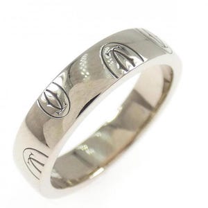 Puede incluir: Un anillo de banda de metal plateado pulido que presenta un motivo grabado repetitivo de un emblema estilizado que se asemeja a una corona o una flor de lis. El anillo tiene una superficie lisa y reflectante con un ancho constante.
