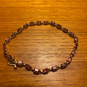 Puede incluir: Un brazalete de oro con una fila de piedras ovaladas de color rosa oscuro.