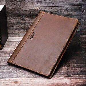May include: A brown leather portfolio with the initials "MGH" embossed on the front.