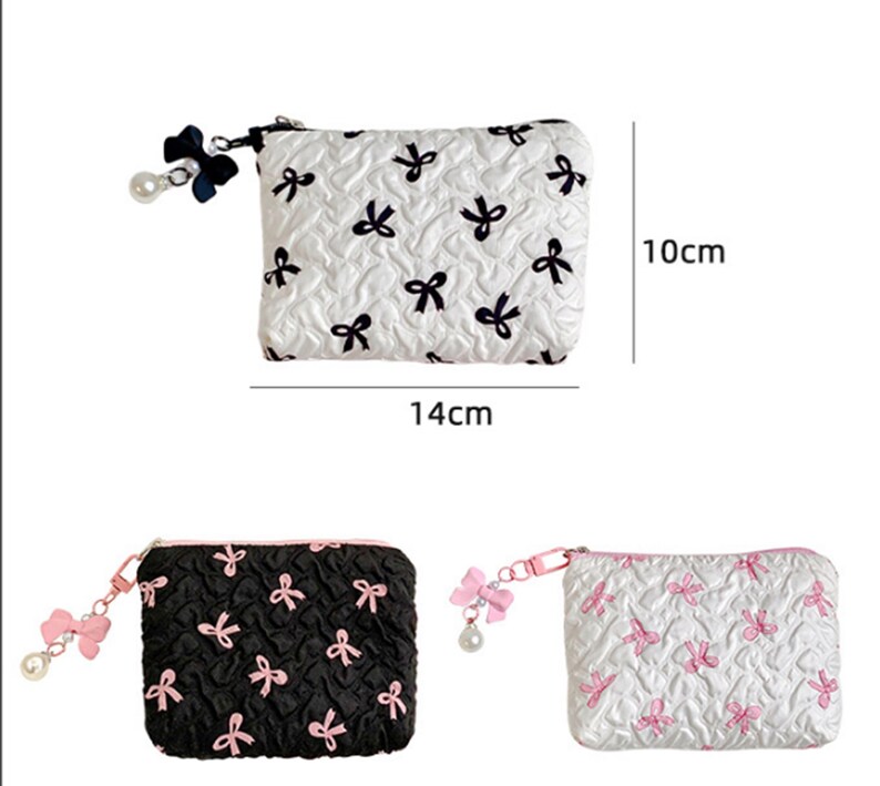 Op de afbeelding: Een witte, zwarte en roze pouch met strikpatroon en ritssluiting. De pouch is 14 cm lang en 10 cm hoog. De pouch heeft een strik- en parelbedel aan de rits. Extra pouches in zwart en wit worden ook getoond.