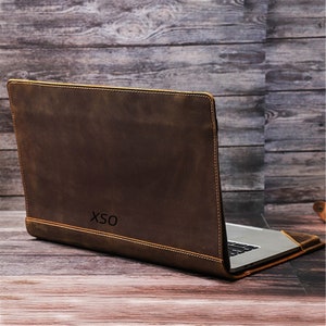 May include: A brown leather laptop sleeve with the initials "XSO" embossed on the front. The sleeve is closed and the laptop is visible inside.