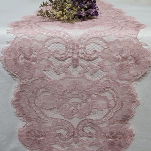 May include: A delicate pink lace table runner with a floral pattern. The lace is intricate and has a soft, romantic feel.