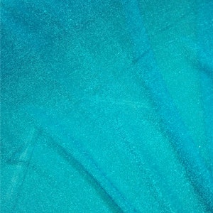 May include: A close-up of a turquoise blue fabric with a sparkly, glittery texture. The fabric is folded and has a slight sheen.