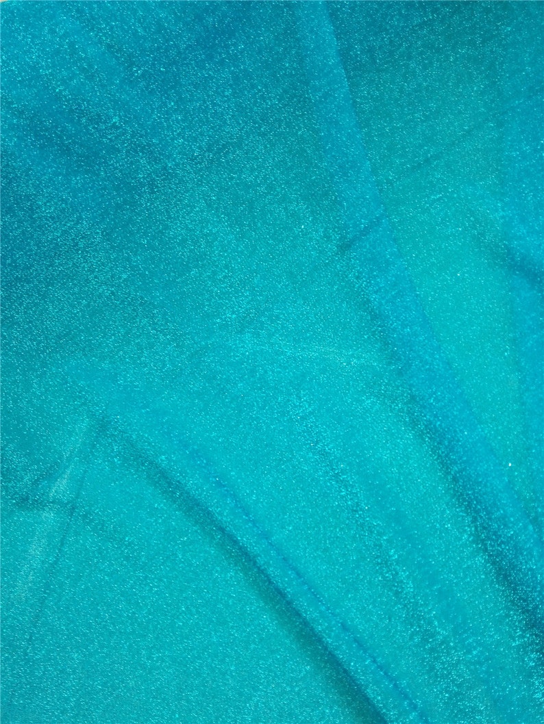May include: A close-up of a turquoise blue fabric with a sparkly, glittery texture. The fabric is folded and has a slight sheen.